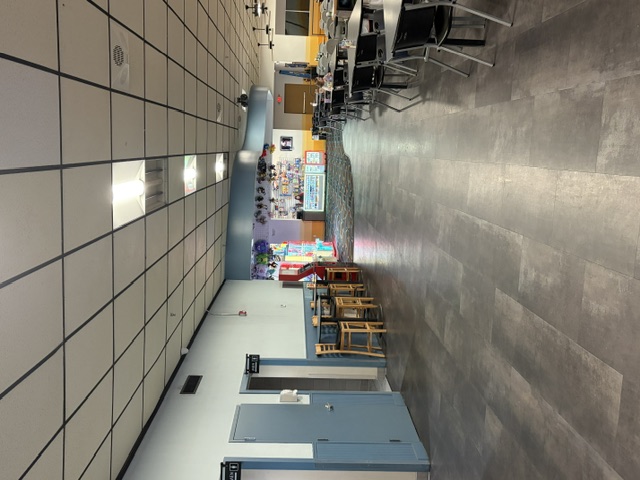 An interior hallway of a bowling center with dark tile floors, dining tables, and a plush toy redemption prize wall.