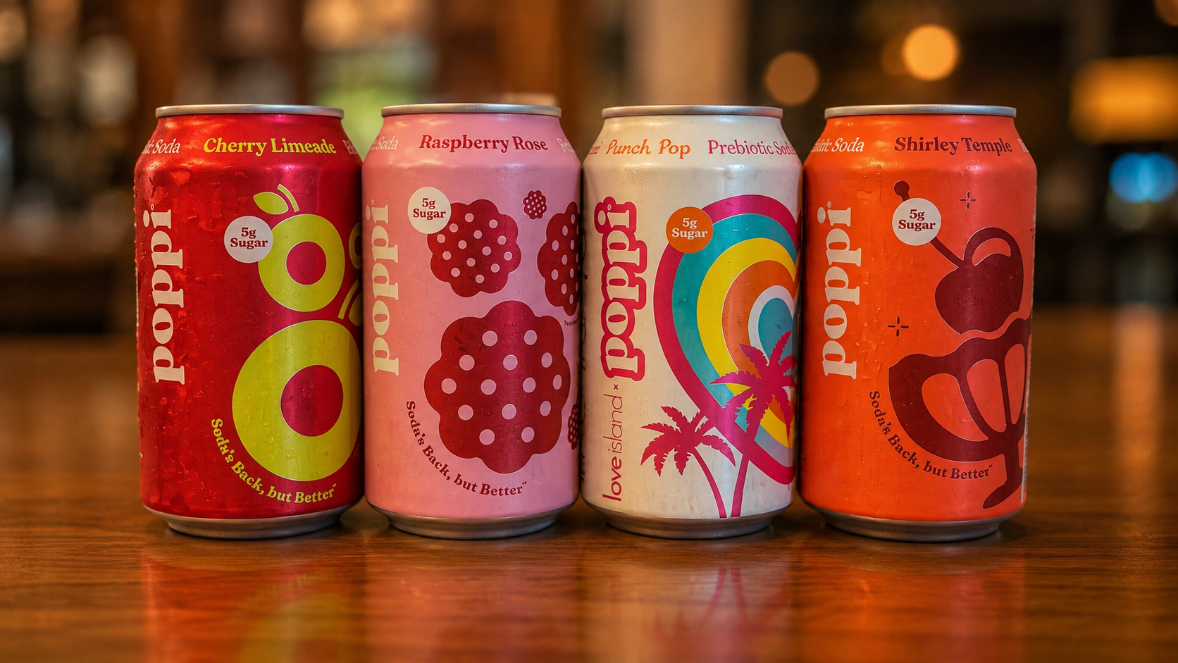 Four cans of Poppi prebiotic soda in different flavors sitting on a wooden bar top.