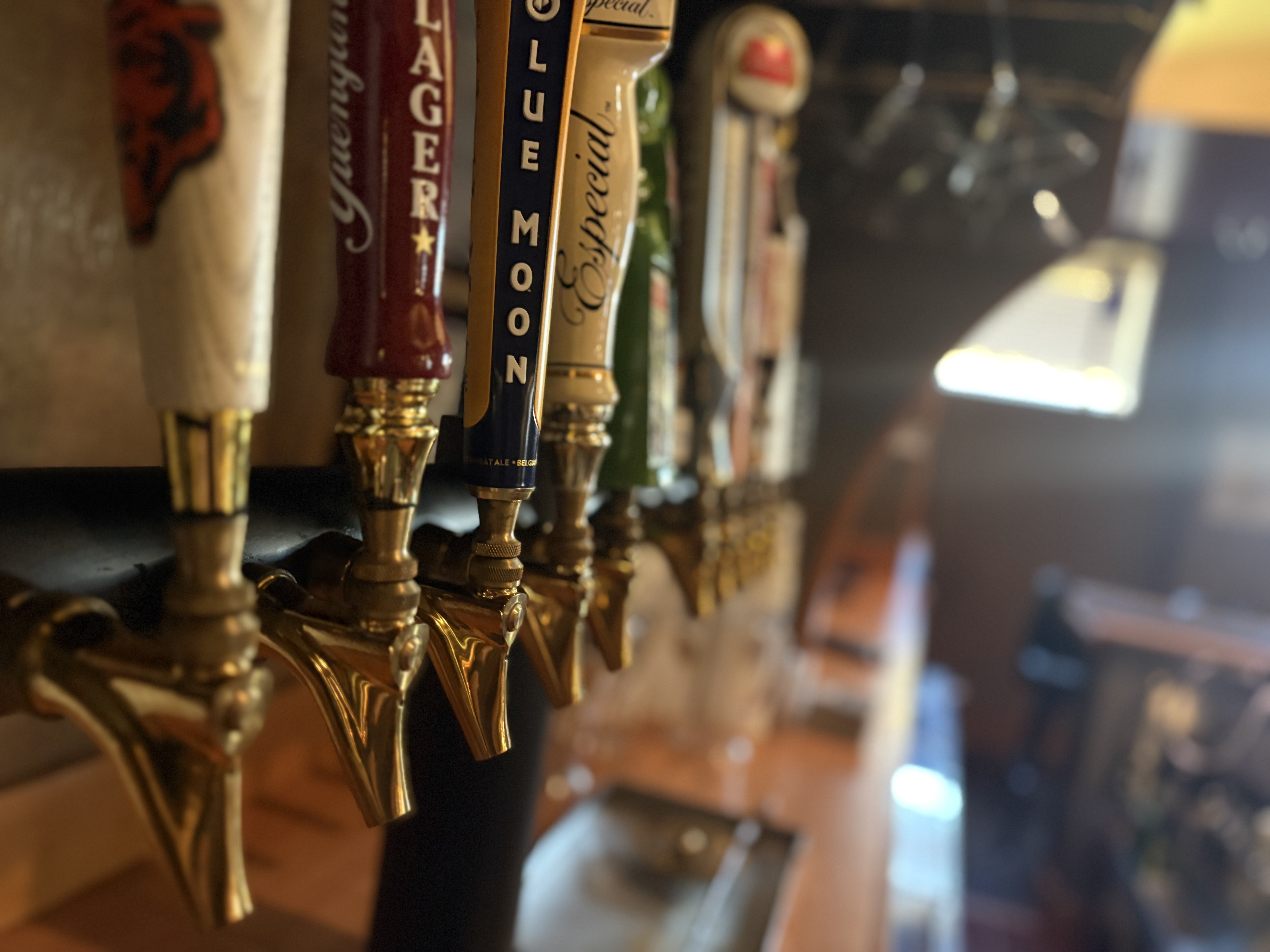 Close-up of several beer tap handles including Yuengling Lager, Blue Moon, and Especial at a bar.